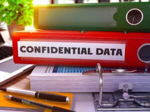 A red binder labelled "Confidential Data" is stacked with other binders and documents on a table surface.