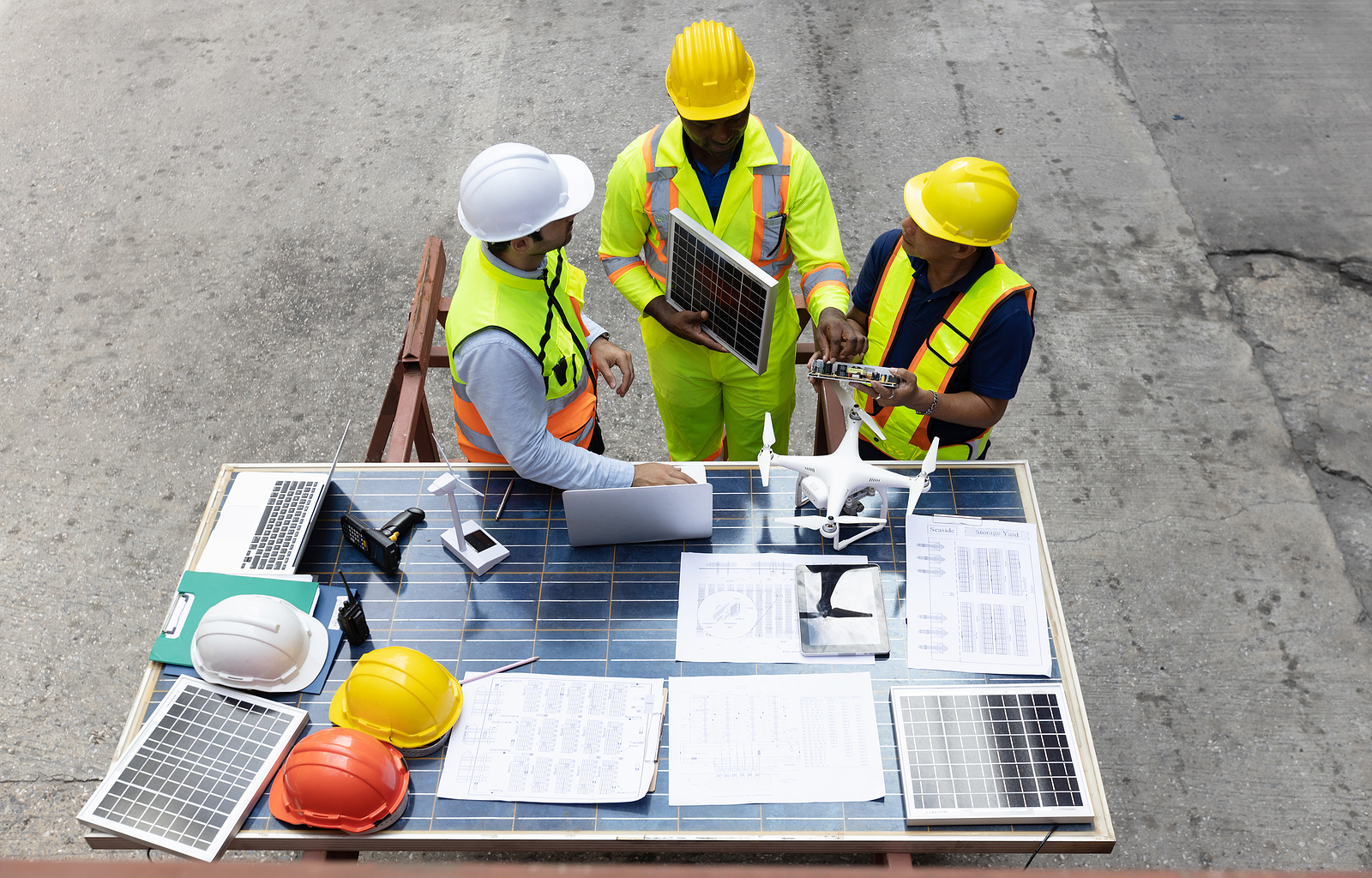 Employees at a manufacturing facility have a discussion next to a work table filled with papers and equipment.