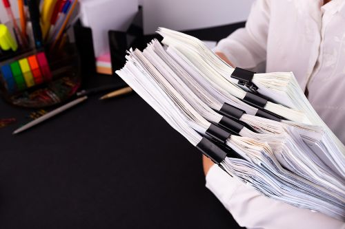 A business person is carrying an armload of documents through an office.